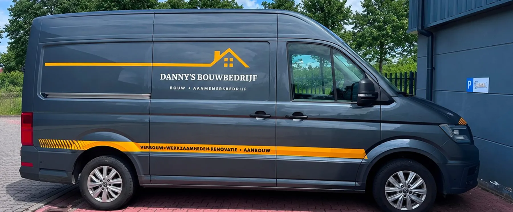 Grijze bedrijfsbus van Danny’s Bouwbedrijf met het logo en een gele streep met de tekst verbouw, werkzaamheden, renovatie en aanbouw