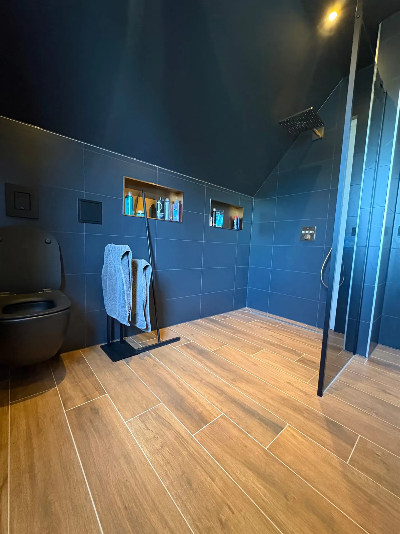 Door Danny’s Bouwbedrijf opgeleverde badkamer met donkerblauw tegelwerk, houtlook vloertegels en inloopdouche