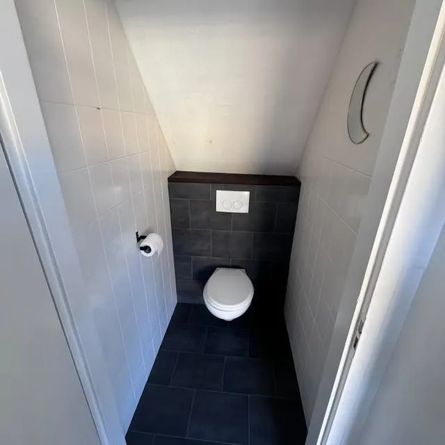 Gerenoveerd toilet met antracietkleurige tegelwand, houten blad en hangend closet